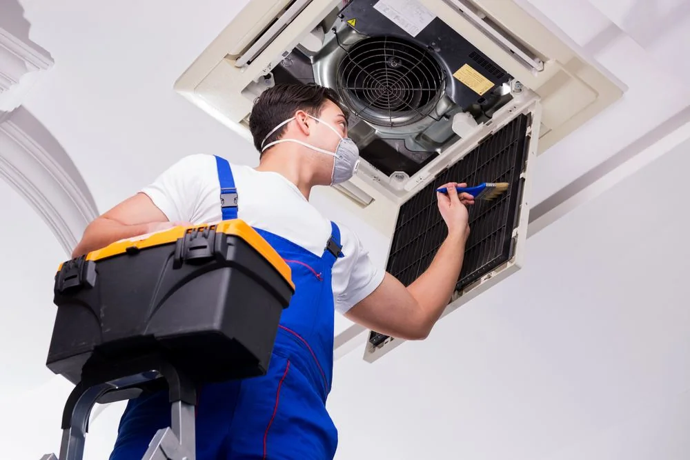 Technician model cleaning an indoor ceiling-mounted HVAC unit